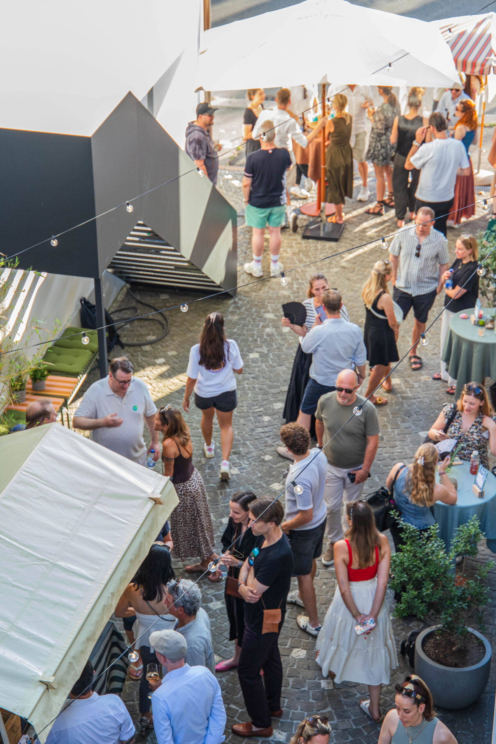 Gäste an sommerlichem Anlass unter Sonnenschirmen in einem Innenhof