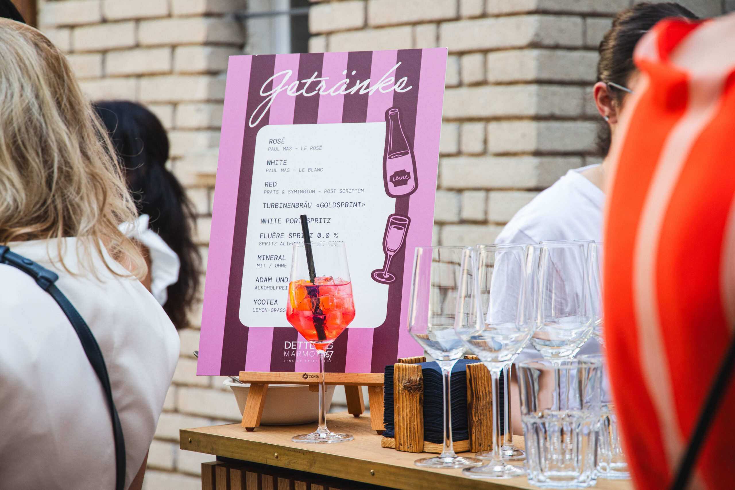Oranger Cocktail vor Getränkekarte und gestapelten Gläsern